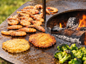 Crevettes, galettes dorées et légumes cuisinés sur la plancha du brasero Le Conifer